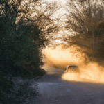 Vehicle driving on an unpaved road generating dust, highlighting dust pollution and the need for effective road dust control.